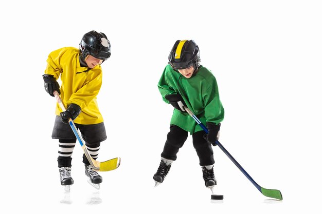 Kleine hockeyspelers met de stokken op ijsbaan en witte muur. Sportjongens met uitrusting en helm oefenen. Concept van sport, gezonde levensstijl, beweging, beweging, actie.
