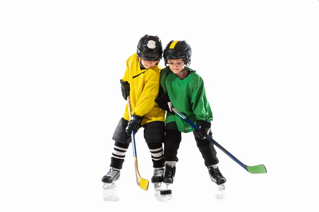 Kleine hockeyspelers met de stokken op ijsbaan en witte studiomuur