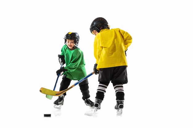 Kleine hockeyspelers met de stokken op ijsbaan en witte studiomuur