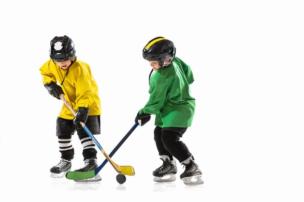 Kleine hockeyspelers met de stokken op ijsbaan en witte studiomuur