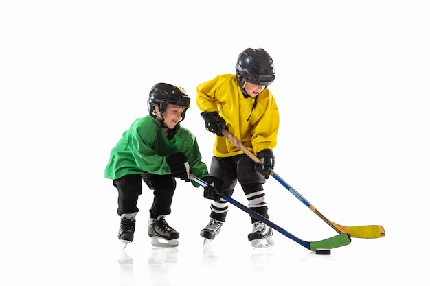 Kleine hockeyspelers met de stokken op ijsbaan en witte studiomuur