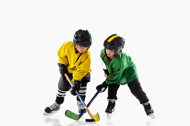 Kleine hockeyspelers met de stokken op ijsbaan en witte studiomuur