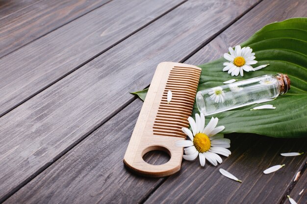 Kleine houten kam ligt op een groot groen blad met een klein glazen flesje