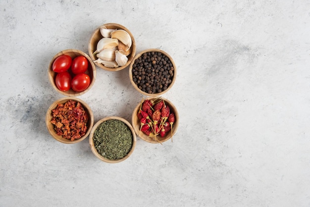 Gratis foto kleine houten kommen met kruiden en tomaten op marmeren achtergrond.