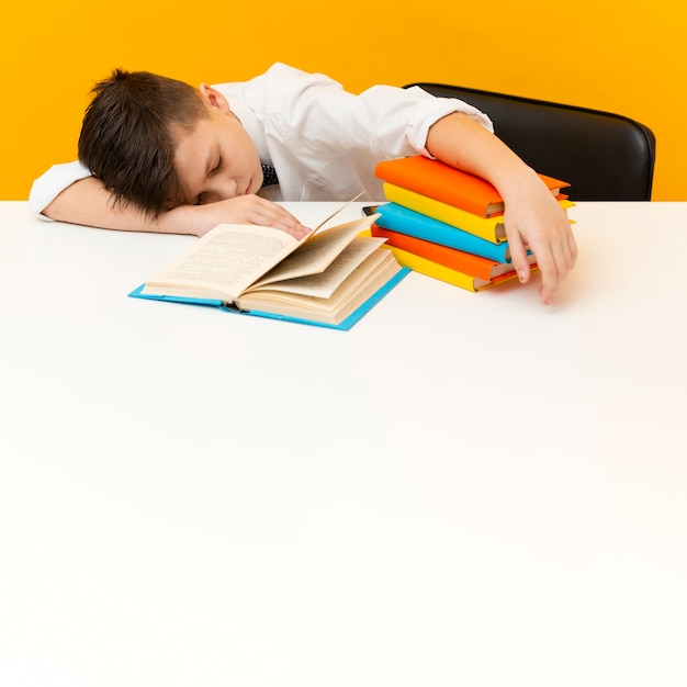 Kleine jongen aan een bureau met stapel boeken