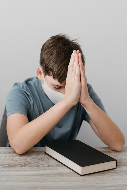 Kleine jongen bidden terwijl het dragen van een medisch masker