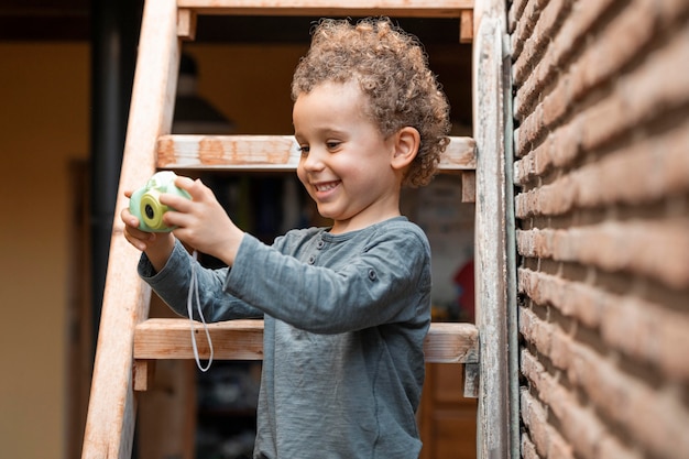 Gratis foto kleine jongen buitenshuis met camera speelgoed