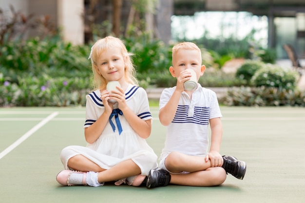 Kleine jongen en meisje drinken en zittend op de grond