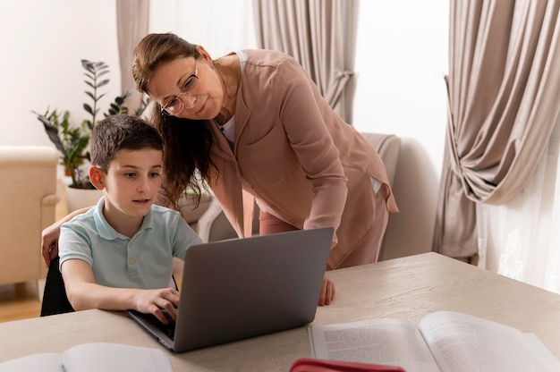 Kleine jongen huiswerk met zijn grootmoeder op laptop