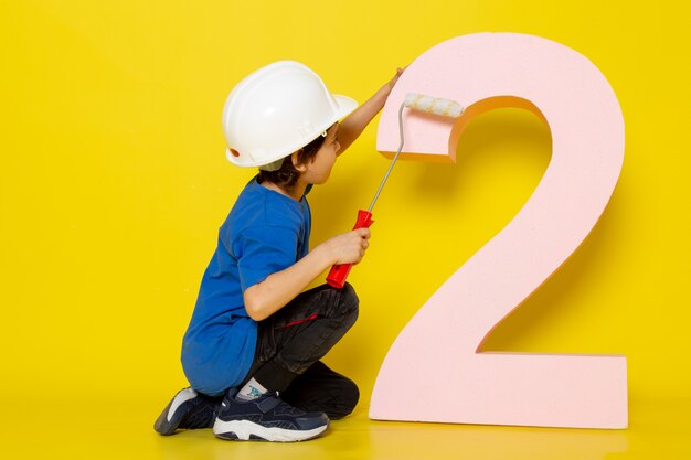 kleine jongen in blauw t-shirt witte helm rond cijfer op gele muur