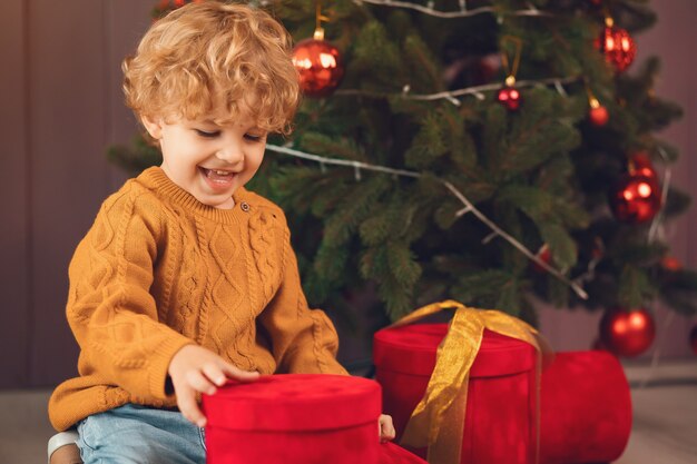 Kleine jongen in de buurt van de kerstboom in een bruine trui