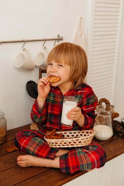 Kleine jongen kerstkoekjes eten en consumptiemelk