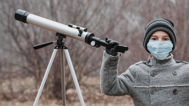 Kleine jongen met medisch masker met behulp van een telescoop