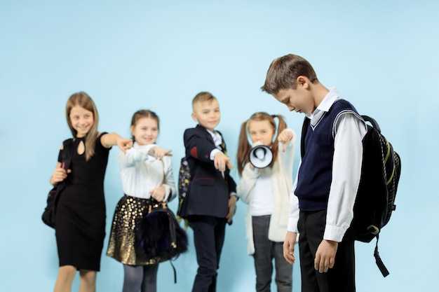 Kleine jongen staat alleen en lijdt aan pesten terwijl kinderen in de muur spottend