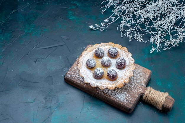 Kleine lekkere cake met suikerpoeder en kersen op donkerblauw bureau, fruitcake koekjes zoet