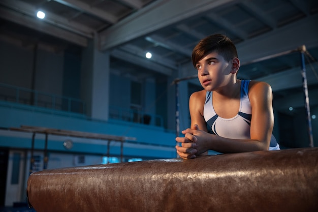 Kleine mannelijke turnster training in de sportschool, flexibel en actief. Kaukasische fit kleine jongen, atleet in witte sportkleding zelfverzekerd posten.