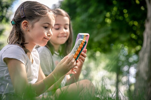 Kleine meisjes buiten met telefoons in een hoesje met puistjes pop it, een trendy anti-stress speeltje.