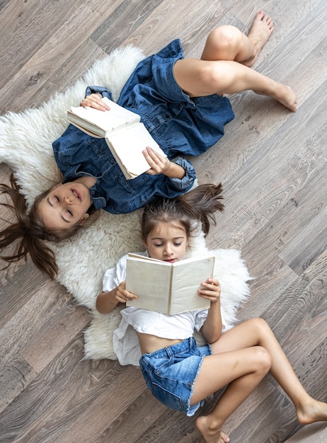 Kleine meisjeszusters lezen boeken die op de vloer liggen, bovenaanzicht.