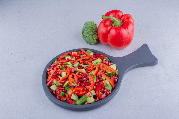 Kleine pan van groentesalade naast een paprika en een broccoli op marmeren achtergrond.
