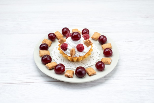 kleine romige cake met frambozen en kleine koekjes op wit-licht