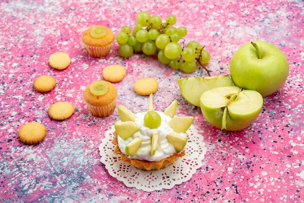 kleine romige cake met gesneden fruit koekjes druiven op gekleurd bureau, zoete cake bakken