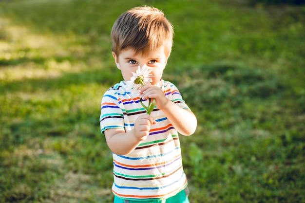 Kleine schattige jongen ruiken een bloem in de zomertuin en ziet er gelukkig uit.