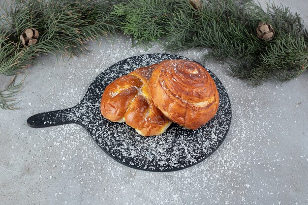 Kleine serveerplank met twee broodjes naast pijnboomtakken op marmeren ondergrond