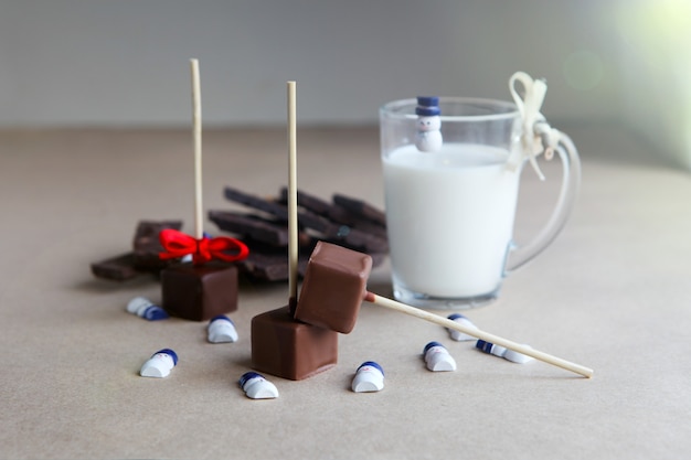 Kleine sneeuwmannen in de buurt van chocoladeblokjes op een stokje met melkbeker en aromatische cacao en chocolade op bruine achtergrond, close-up