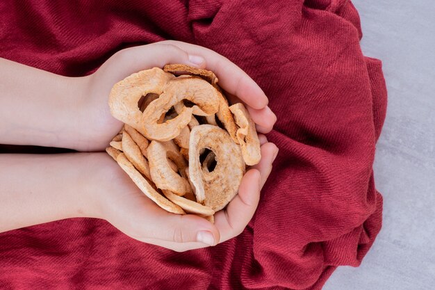 Kleine stapel van gedroogde appelschijfjes gehouden in tot een kom gevormde handen op witte achtergrond.