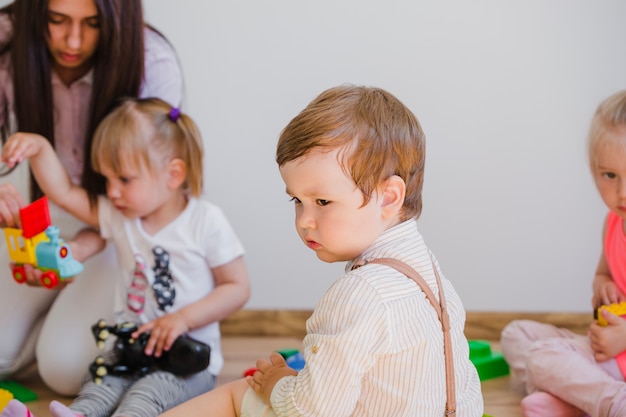 Kleine stijlvolle jongen die op de vloer zit