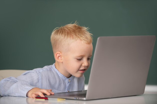 Kleine student jongen met behulp van laptopcomputer in de klas grappige blonde leerling op blackboard