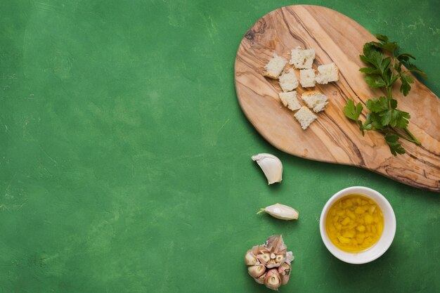 Kleine stukjes brood; peterselie; knoflook en kom met gegoten olijfolie op groene gestructureerde achtergrond