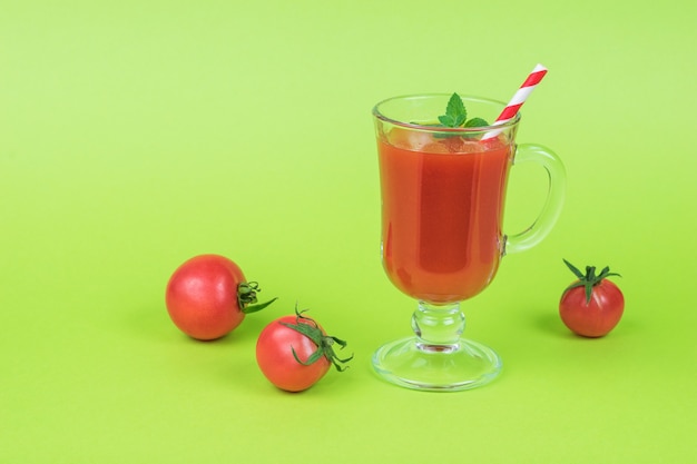 Kleine tomaten en een glas tomatensap op een groene achtergrond.