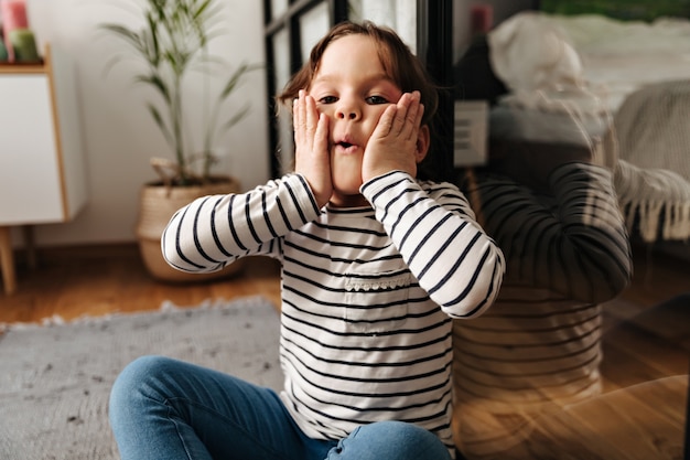 Kleine vrouw ploetert en blaast haar wangen. Portret van kind zittend op de vloer.