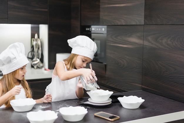 Kleine zusters het deeg voorbereiden voor het maken van cookies in de keuken