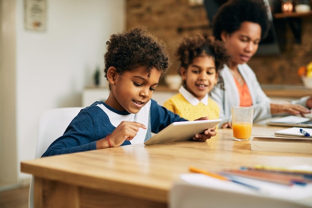 Kleine zwarte jongen die thuis op het net surft op digitale tablet