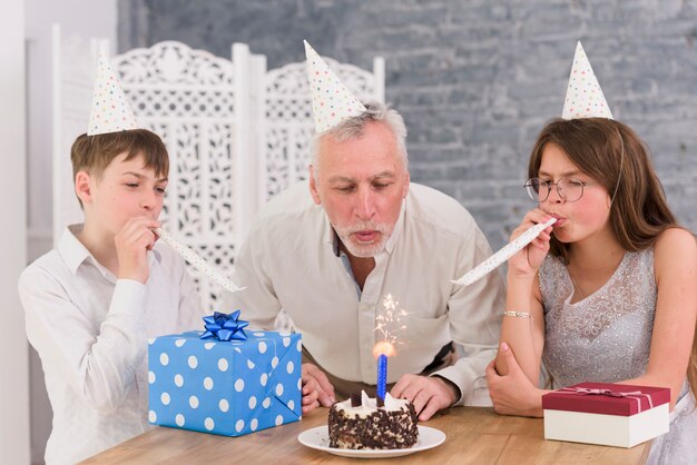 Kleinkinderen blazende partijhoornen met hun grootvader blazend sterretje op verjaardagscake