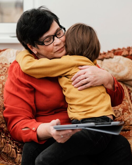 Kleinzoon knuffelen zijn grootmoeder terwijl ze een tablet vasthoudt