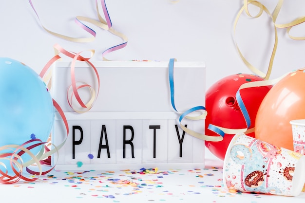Kleurrijke ballonnen met papieren confetti en een led-lampbord met [PARTY] erop geschreven