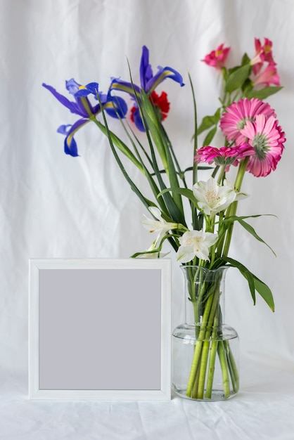 Kleurrijke bloemen in bloemenvaas met leeg fotokader op wit gordijn