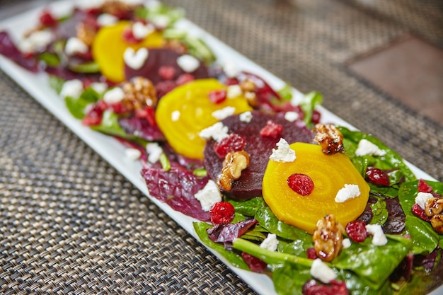 Kleurrijke rode en gele bietensalade met witte fetakaas op een bedje van groen op een lang bord