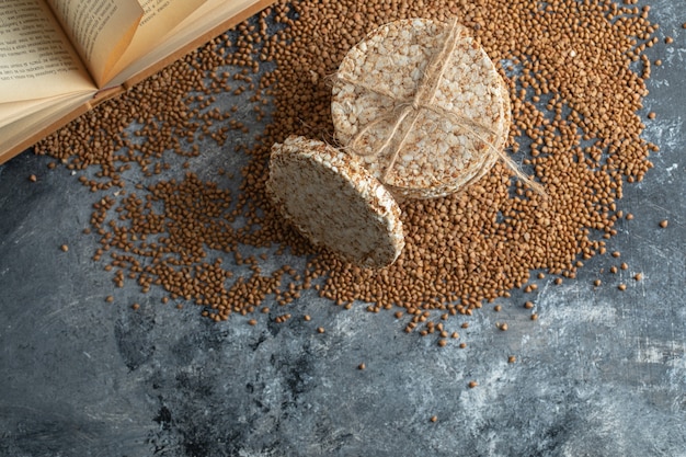 Knäckebröd, ongekookt boekweit en boek op marmeren oppervlak