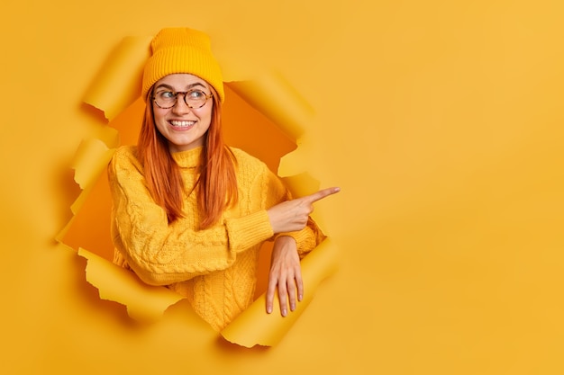 Gratis foto knap vrolijk duizendjarig meisje met een tedere glimlach wijzend op kopie ruimte