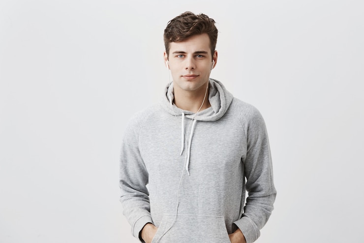 Gratis Foto knappe aantrekkelijke europese man in grijze hoodie, met de handen in de zakken, ziet er tevreden uit, heeft een goed humeur als thuiskomt na het werk. knappe mannelijke student vormt.