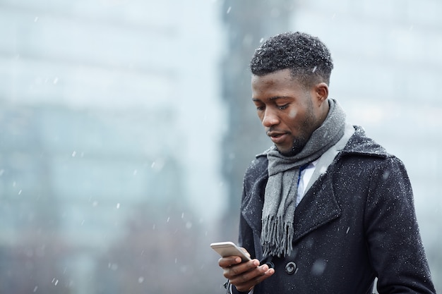 Knappe Afrikaanse man met smartphone in sneeuw