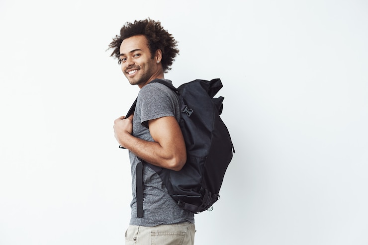 Gratis Foto knappe afrikaanse mens met rugzak glimlachen die zich tegen witte muur klaar gaan wandelen of een student op weg naar universiteit.