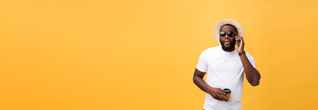 Knappe Afro-Amerikaan met mobiele telefoon en koffiekopje meenemen geïsoleerd over geelgouden backg