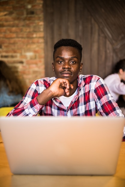 Knappe afro-amerikaanse man in casual kleding met een kopje koffie en laptop gebruikt.