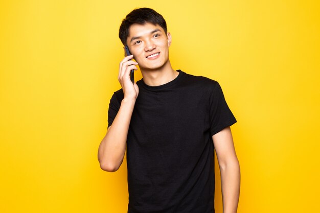 Knappe Aziatische jonge man praten over de telefoon op gele muur