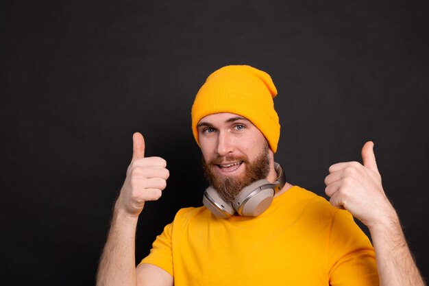 Knappe bebaarde hipster man gele hoed t-shirt met koptelefoon geïsoleerd op zwarte achtergrond